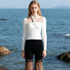 Front view shows the slash-neck frame and halter twist detail, paired with high-waist trousers for a clean, modern silhouette.