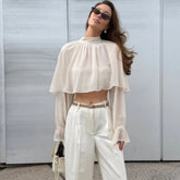 Model in a white chiffon top with cape overlay and gathered crew neckline, creating soft volume across the shoulders and chest.