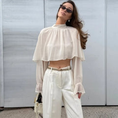 Model in a white chiffon top with cape overlay and gathered crew neckline, creating soft volume across the shoulders and chest.