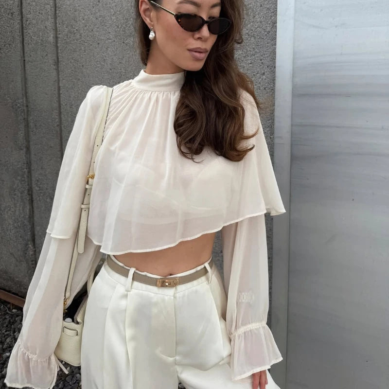 Relaxed white chiffon top styled with high-rise pants and sunglasses, balancing a minimal silhouette with a softly dramatic neckline.