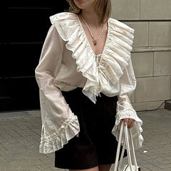 A person wearing a white ruffle lace-up summer shirt styled for office lady elegance and black shorts, holding a white bag on a sidewalk.