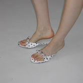 White sandals with black polka dots worn by a person on a gray background