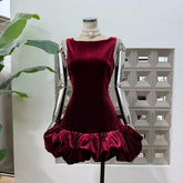 Mannequin wearing a wine-toned velvet sleeveless mini dress with a dramatic cloud bubble hem in a bright studio setting.