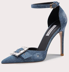 Blue denim high-heeled shoe with a decorative buckle on a light gray background