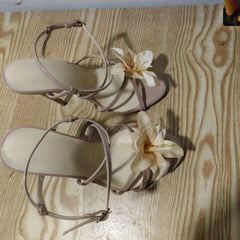 Pair of beige sandals with floral decorations on a wooden surface