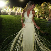 Model in a yellow beaded halter mermaid gown with long fringe strands, captured outdoors under evening lights on grass
