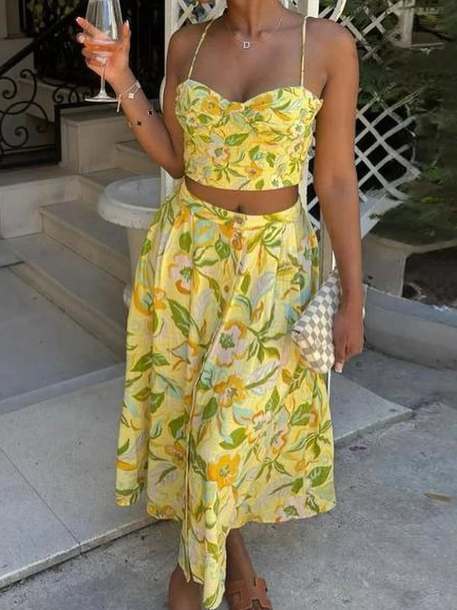 Woman wearing a yellow floral two-piece set styled for a sunny vacation look holding a glass outdoors.
