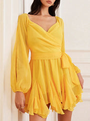 Yellow ruffle mini dress with long sleeves and a tie waist detail, worn by a person against a white background