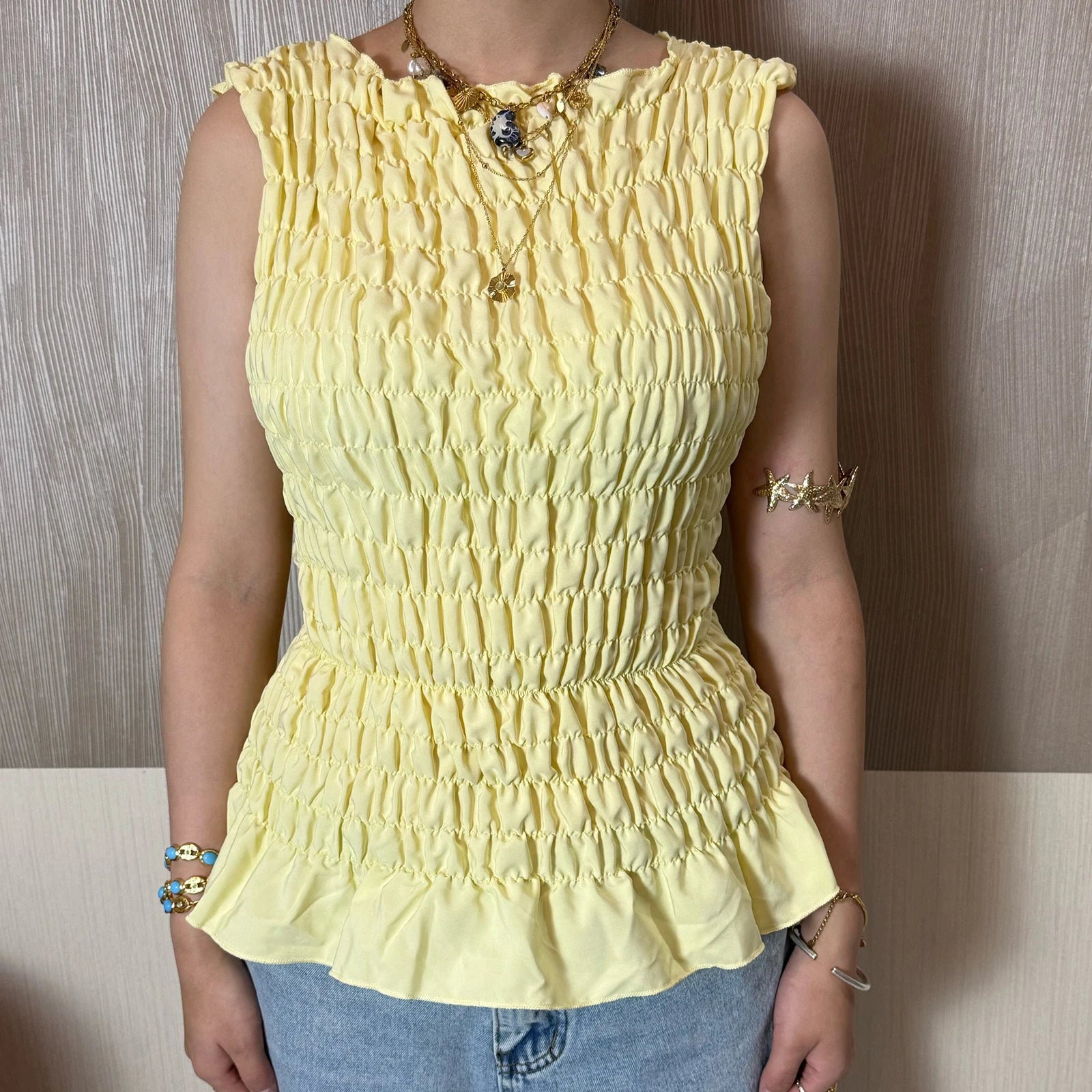 Person wearing Yellow shirred peplum tank top with ruffle hem styled casually with a neutral background