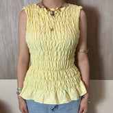 Person wearing Yellow shirred peplum tank top with ruffle hem styled casually with a neutral background