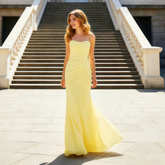 Model wearing a yellow strapless satin mermaid gown with pleated bodice in front of an elegant building