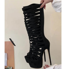 Black high-heeled boot with strappy design held by a hand against a neutral background