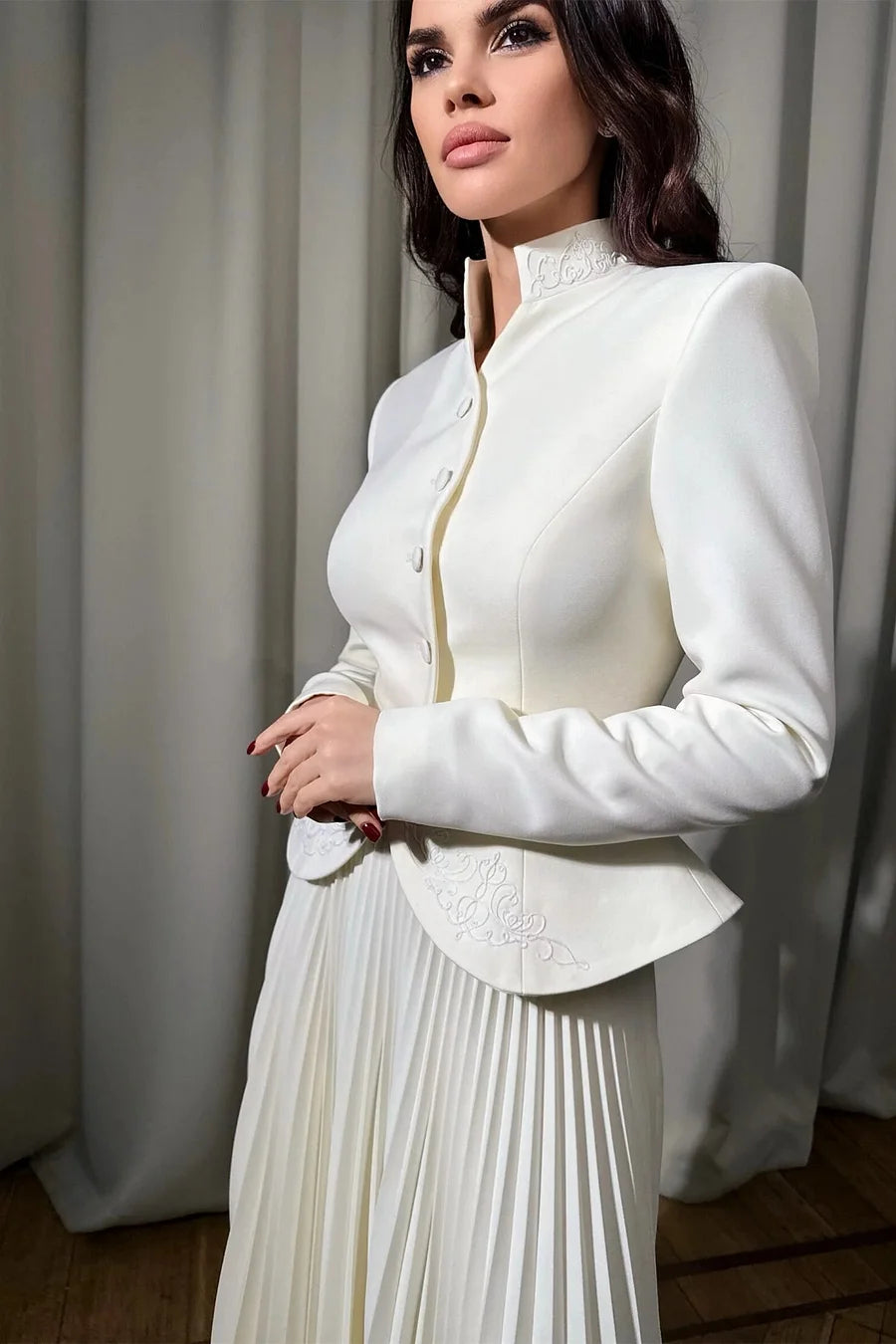 Woman wearing a white outfit with a pleated skirt against a neutral background