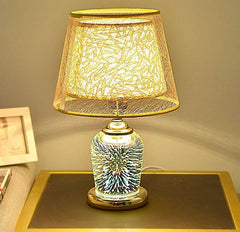  Golden Atelier 3D fireworks table lamp with a glass enclosure filled with intricate lighting elements that create a 3D fireworks effect. The lamp has a base with up-down lighting controls, displayed on a table in a living room setting. Yellow