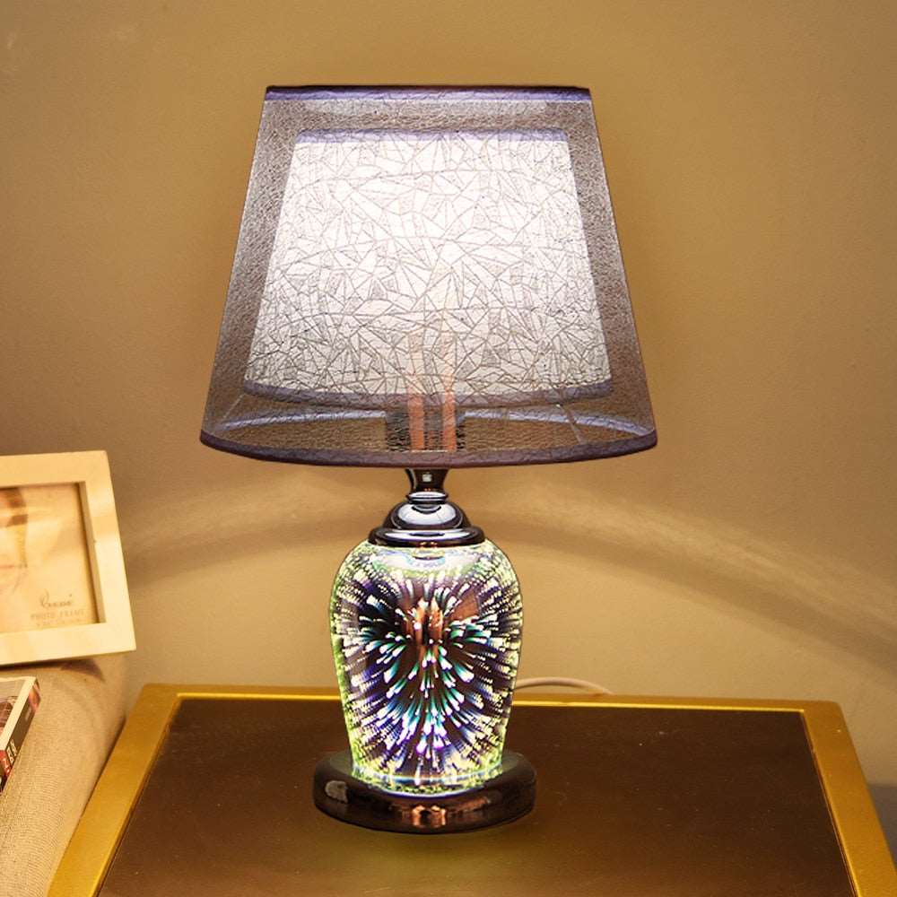  Golden Atelier 3D fireworks table lamp with a glass enclosure filled with intricate lighting elements that create a 3D fireworks effect. The lamp has a base with up-down lighting controls, displayed on a table in a living room setting.  Grey