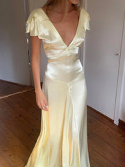 Woman wearing a light yellow evening gown with ruffled sleeves in an indoor setting.