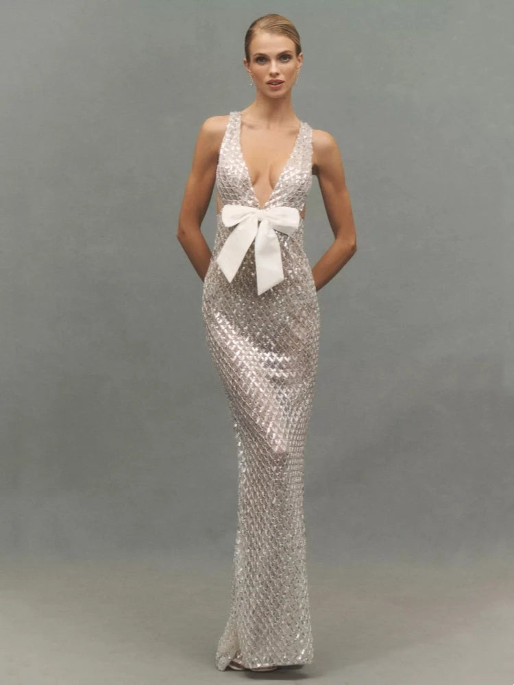 Model posing in a silver sequined V-neck gown with a white bow.