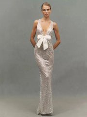 Model posing in a silver sequined V-neck gown with a white bow.