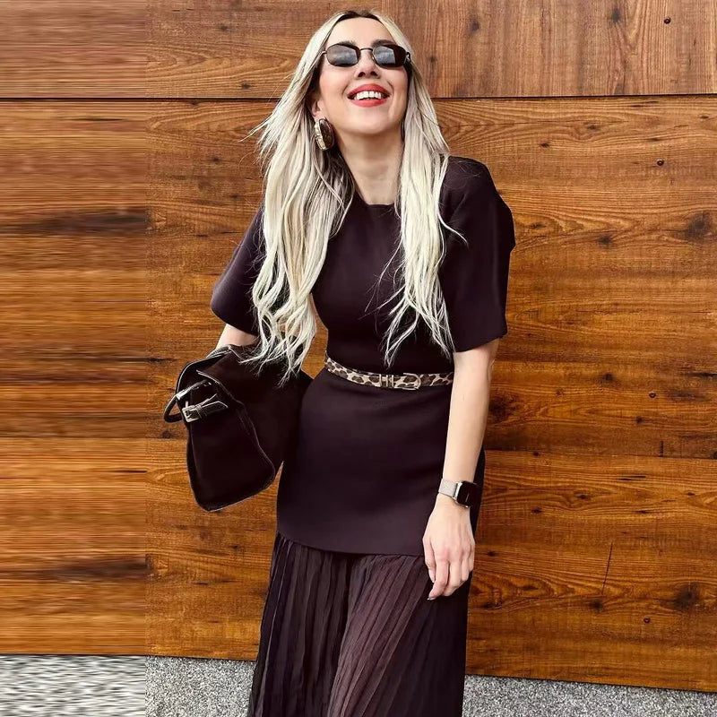 Woman in a dark outfit with sunglasses standing against a wooden wall