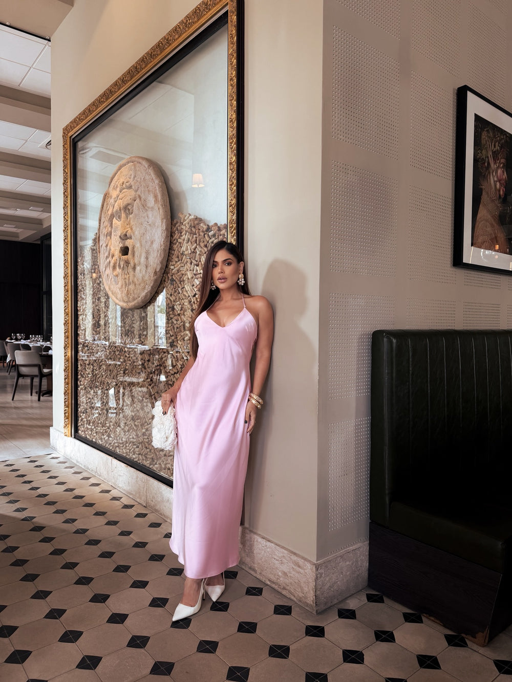 Woman in a pink dress standing in a stylish interior setting with a large mirror and artwork.