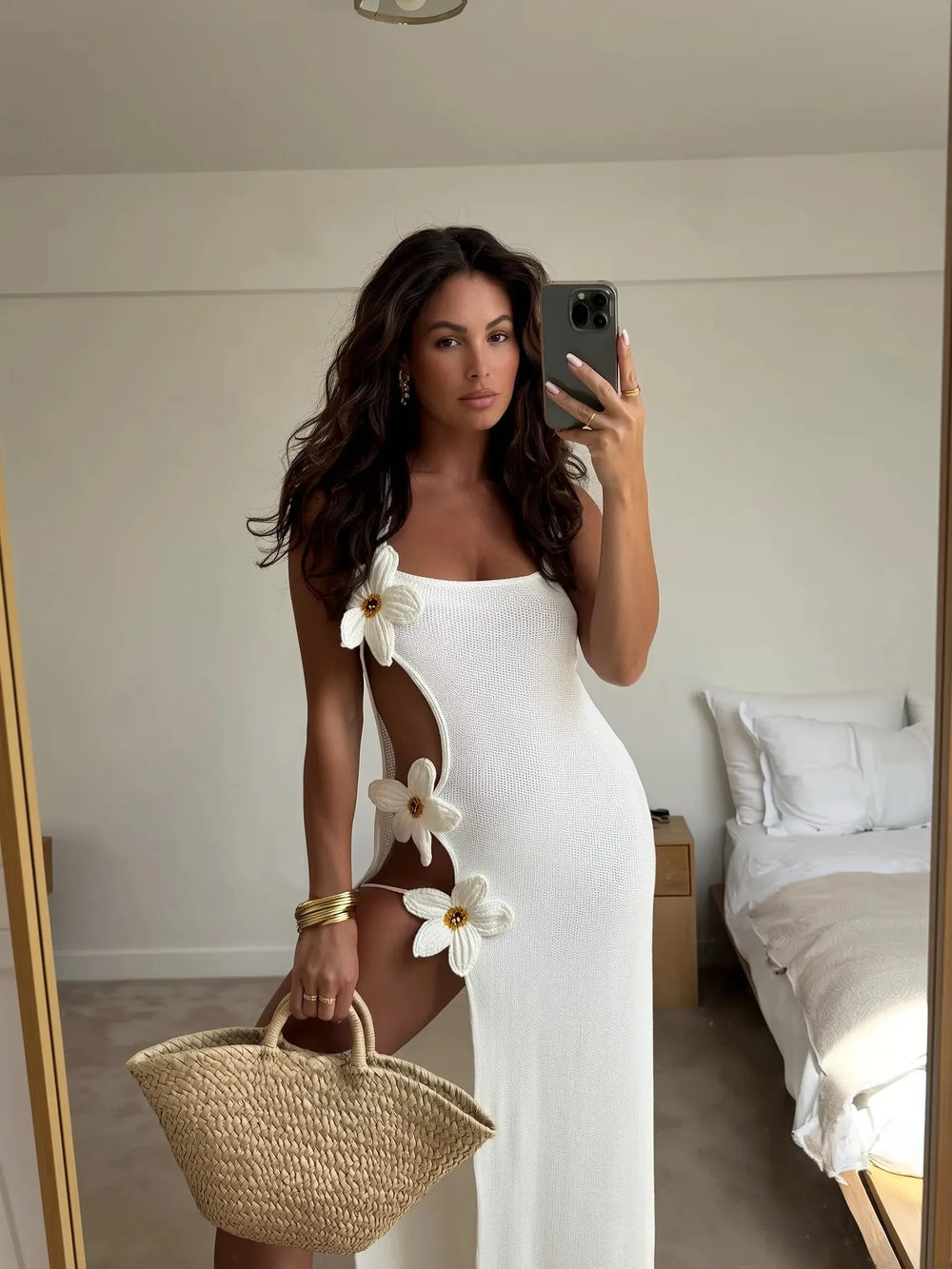 Woman in a white dress with floral details taking a mirror selfie in a bedroom.
