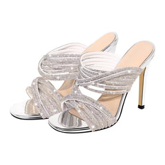 Silver metallic mule sandals with crystal-embellished twisted straps and a stiletto heel.