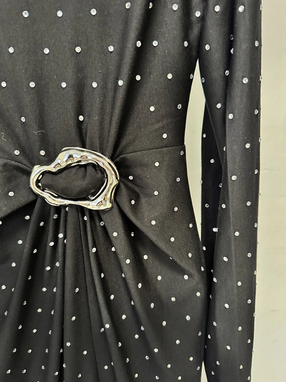 Black polka dot dress with a metallic belt on a neutral background