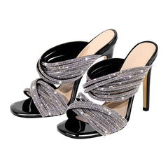 Black patent leather mule sandals with crystal-embellished twisted straps and a stiletto heel.
