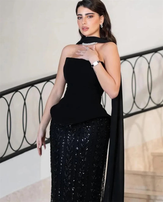 Woman in a black dress with a sequined skirt standing in an elegant interior setting.