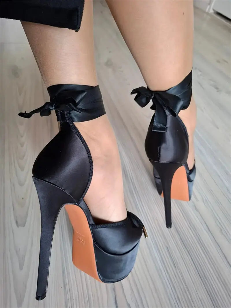 Black high-heeled shoes with bow details on a light wooden floor.