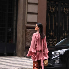 Woman in a pink outfit walking on a city street with a black car and building in the background.