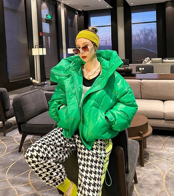  Golden Atelier short puffer jacket in cotton with a big, attached hood, soft padding throughout, and a zipper closure, modeled on a person in a casual outdoor setting. Green