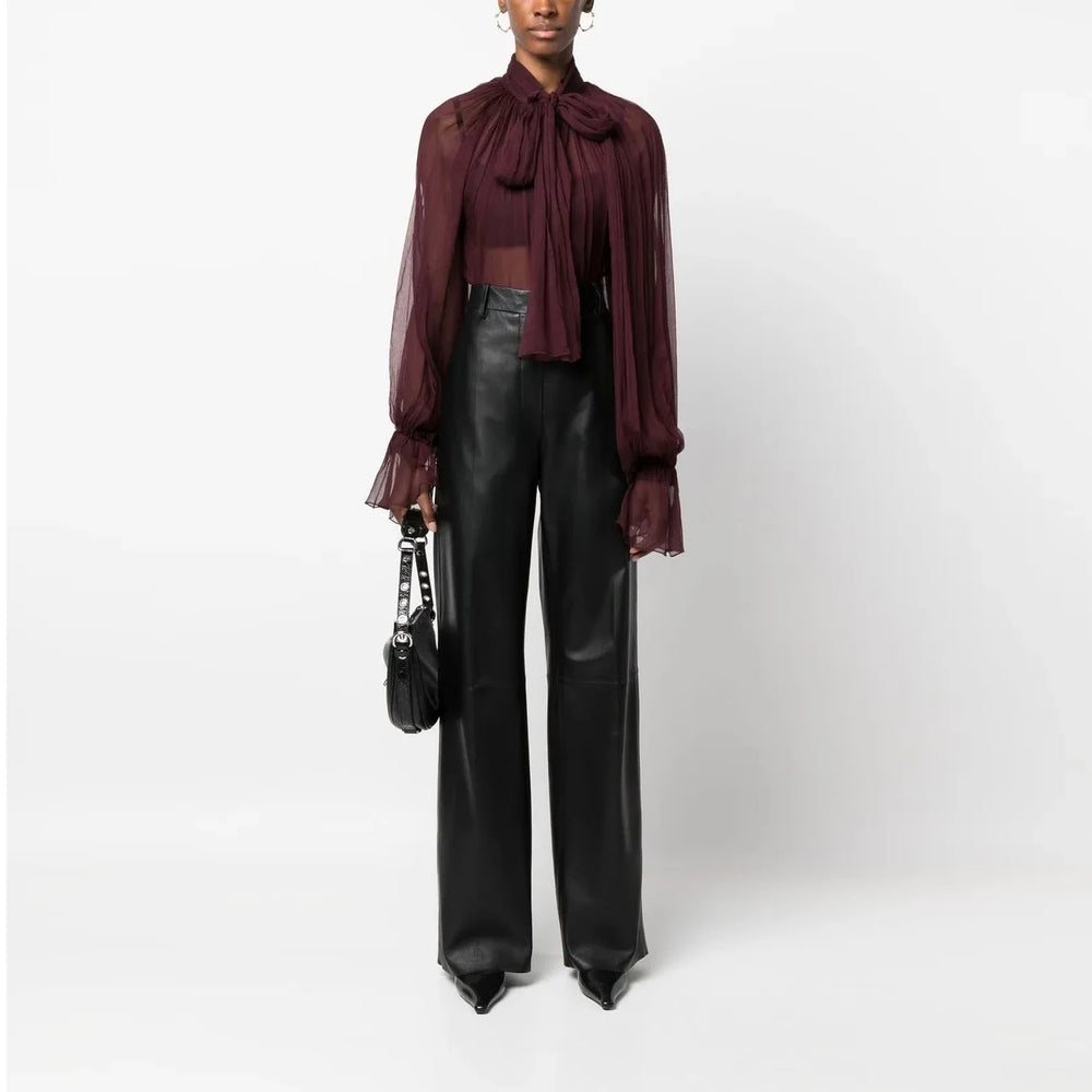Person wearing a burgundy blouse with sheer sleeves and a black leather outfit on a white background