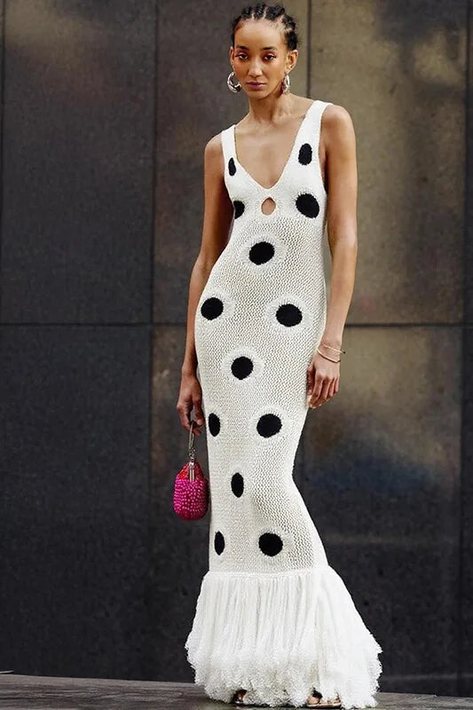 Woman wearing a white dress with black polka dots and ruffled hem, holding a pink handbag.
