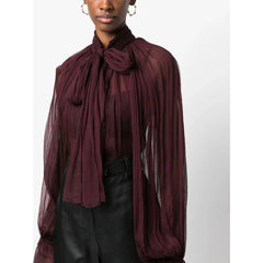Person wearing a burgundy sheer blouse with a tied neckline on a white background