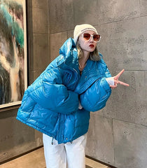  Golden Atelier short puffer jacket in cotton with a big, attached hood, soft padding throughout, and a zipper closure, modeled on a person in a casual outdoor setting. Blue