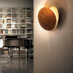 Round wall sconce casting light on a wall with a bookshelf in the background