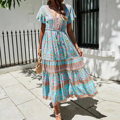 Model holding a straw bag while wearing a tiered midi dress with V-neck and short butterfly sleeves