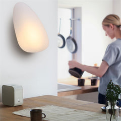 Golden Atelier LED wall lights in a modern glass pebble design, mounted on a wall and casting a warm glow. 