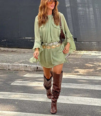 Woman in a light green dress and brown knee-high boots walking on a zebra crossing 