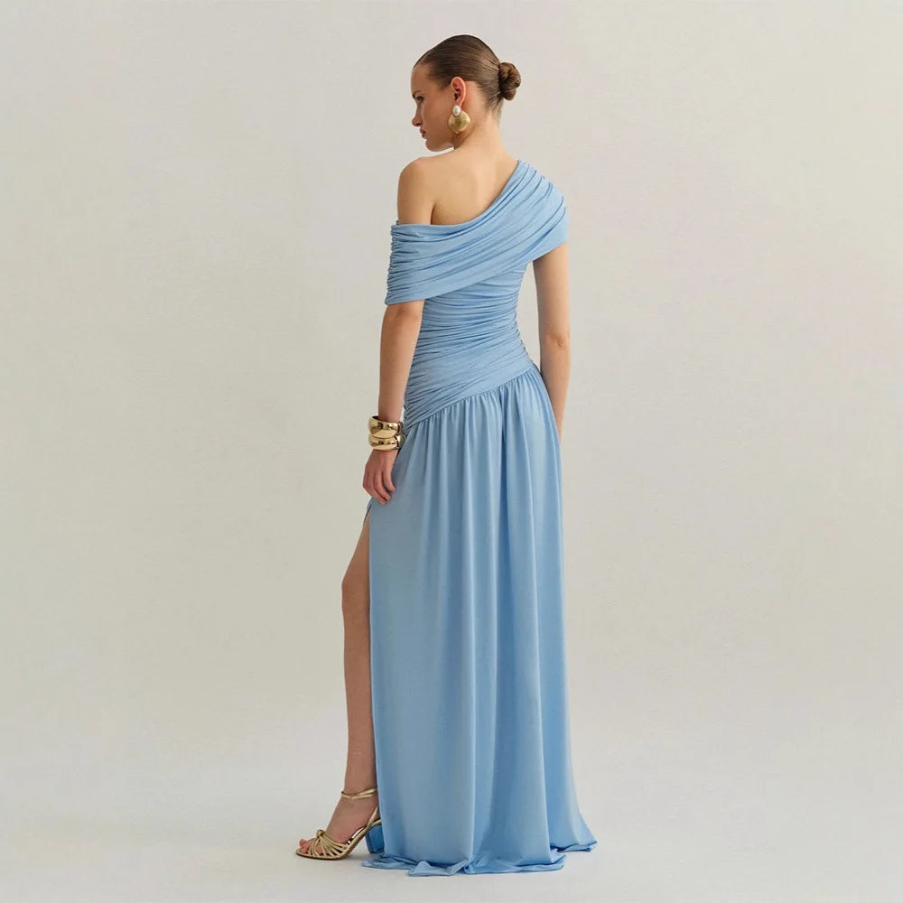 Woman wearing a light blue one-shoulder dress with a slit on a plain background