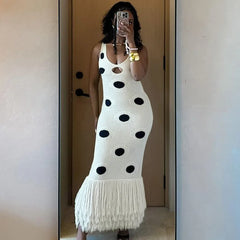 Person wearing a white dress with black polka dots and fringe details, standing in front of a mirror.
