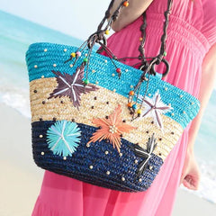 A woman carrying the straw tote bag on her shoulder, enjoying a sunny day at the beach.