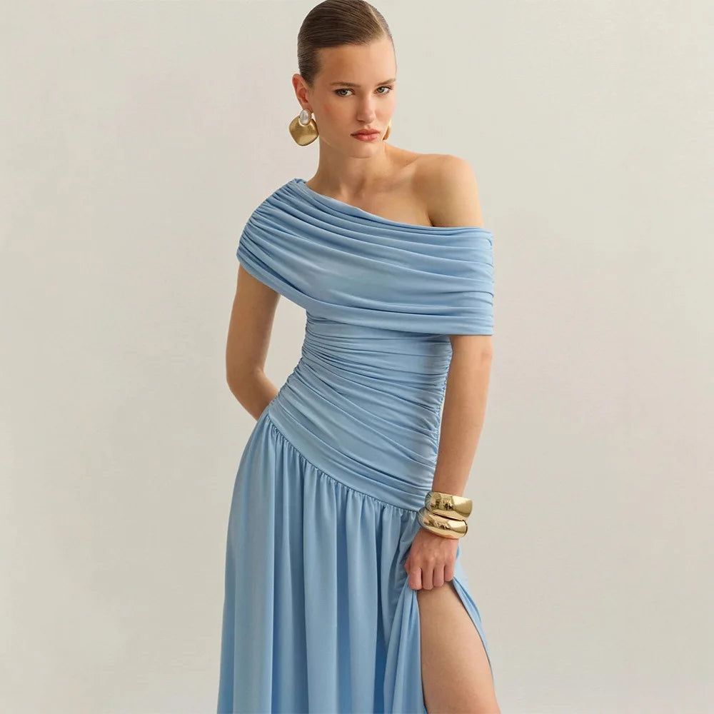 Woman wearing a light blue off-shoulder dress with gold jewelry on a plain background