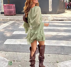 Woman in a green dress and brown knee-high boots crossing a street.
