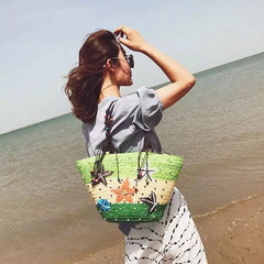 A woman carrying the straw tote bag on her shoulder, enjoying a sunny day at the beach.