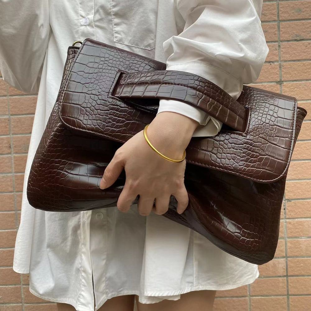 Person holding a brown leather clutch bag against a tiled wall background
