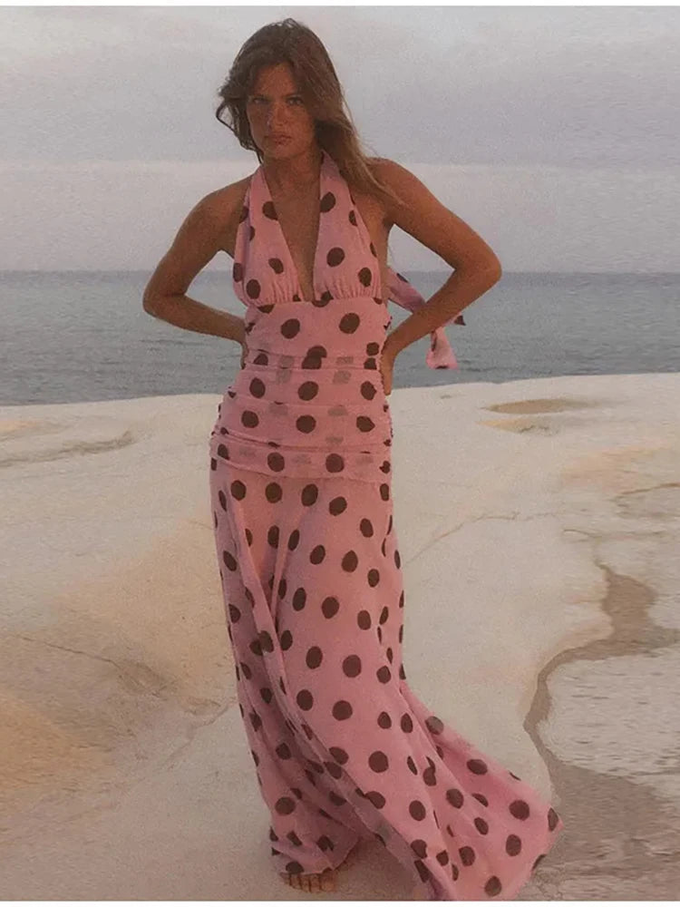 Woman in a pink polka dot dress standing on a beach.