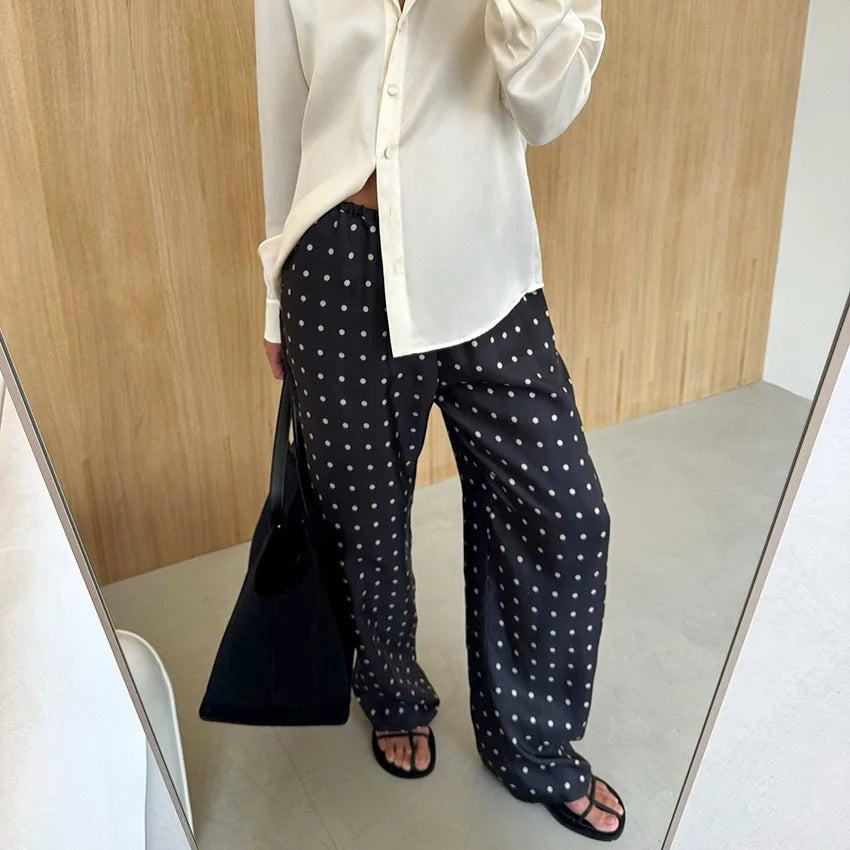 Person wearing a white shirt and black polka dot pants standing in front of a mirror.