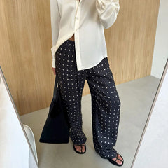 Person wearing a white shirt and black polka dot pants standing in front of a mirror.